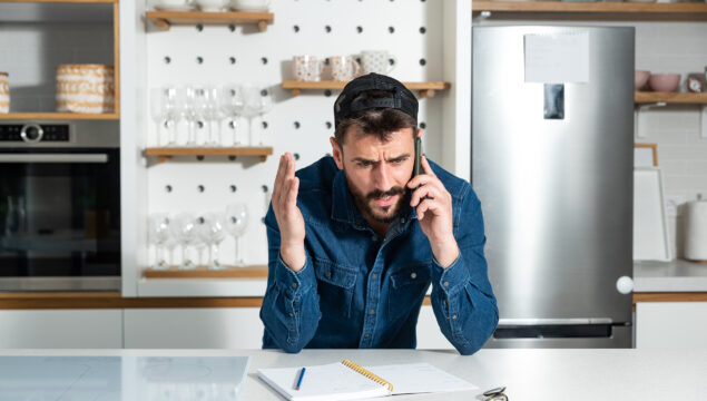 Young angry and frustrated business casual man working at home talking and yelling at the smartphone because delivery company courier is late with his package he ordered online